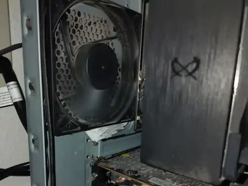 A close photo of the interior of a computer tower, looking toward the rear panel where a fan is fastened to the case.  Wedged below the fan's housing is a thickly-folded stack of white paper.